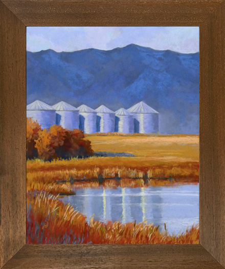 Photo of a pastel painting of six silos with mountains behind and a pond in front. with brown frame.